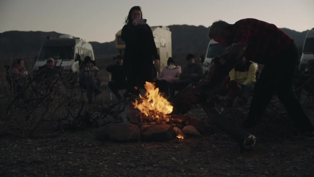 Fogueira à noite com o comboio de motorhomes ao fundo
