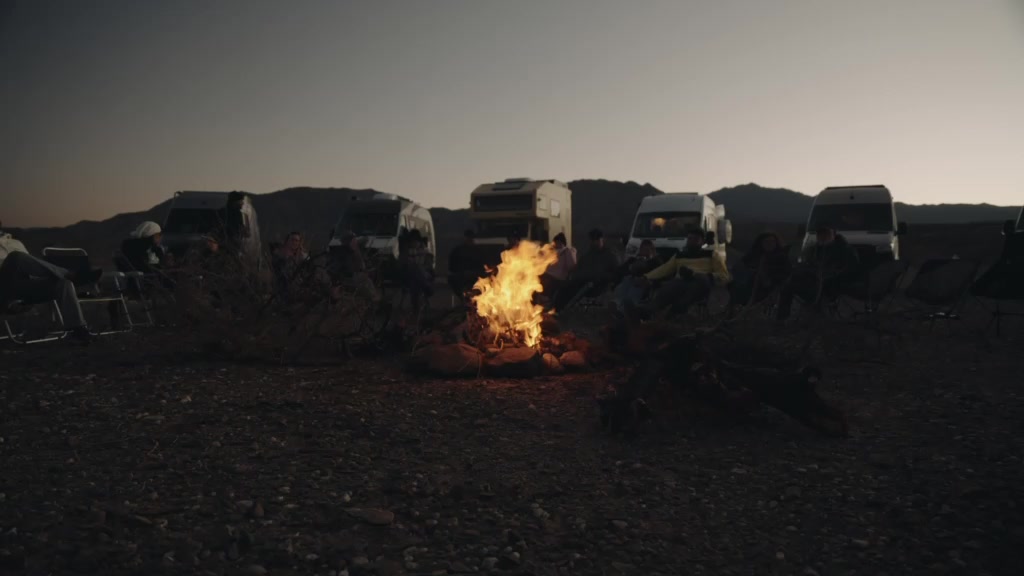 Comboio de motorhomes com fogueira ao entardecer